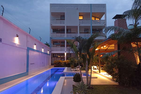 Atardecer en el Residencial Morona Flats & Pool, con piscina 25 m y luces LED y jardines tropicales, sillas largas, maloca y parilla. Flores, fragancias y grillos. Tranquilidad y privacidad.